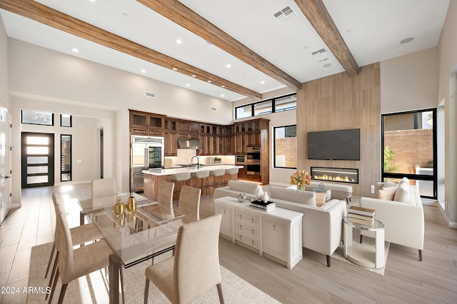 dining space with a high ceiling, visible vents, light wood-type flooring, beam ceiling, and a tiled fireplace