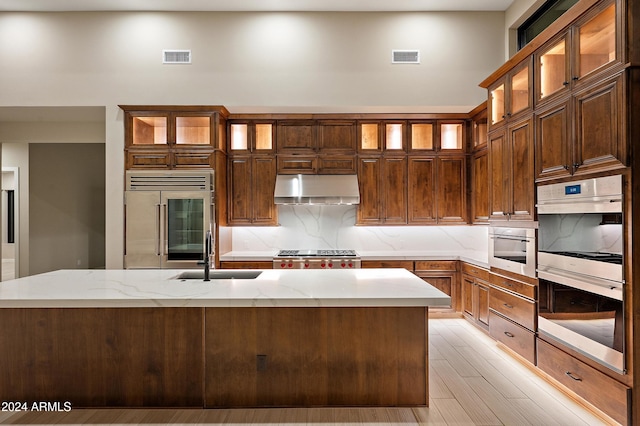 kitchen featuring double oven, under cabinet range hood, built in refrigerator, a sink, and backsplash