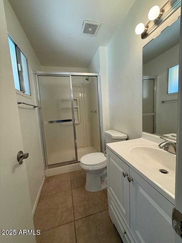 bathroom with tile patterned floors, visible vents, toilet, a shower stall, and vanity