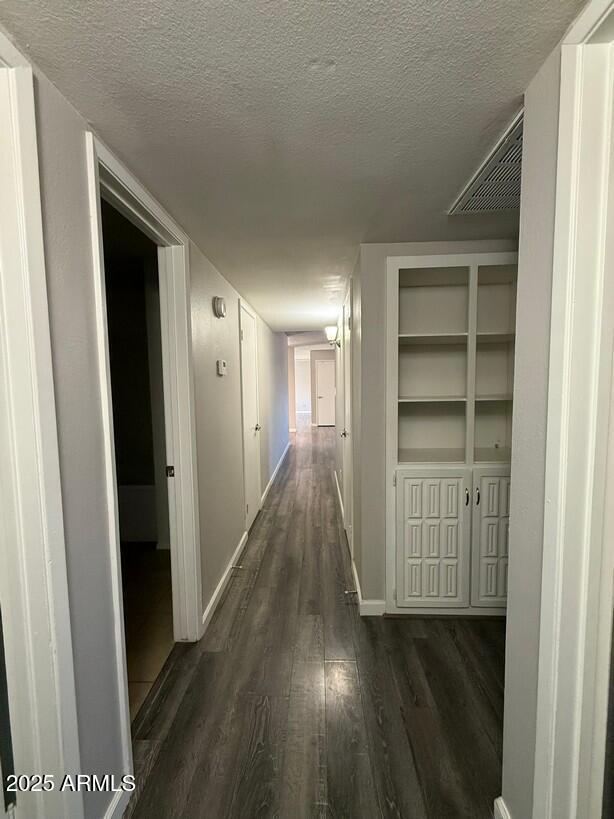 hallway featuring baseboards, a textured ceiling, and dark wood-style flooring