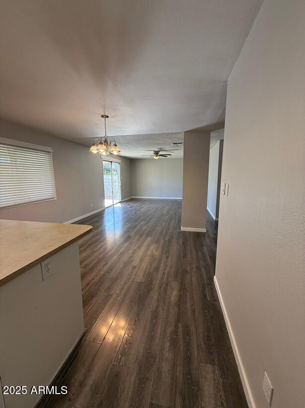 unfurnished dining area featuring dark wood-style floors, ceiling fan with notable chandelier, and baseboards