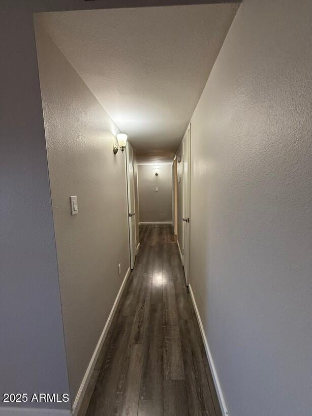 hallway with dark wood-type flooring, baseboards, and a textured ceiling