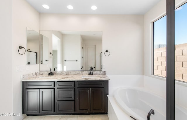 bathroom featuring a garden tub, double vanity, a sink, and recessed lighting