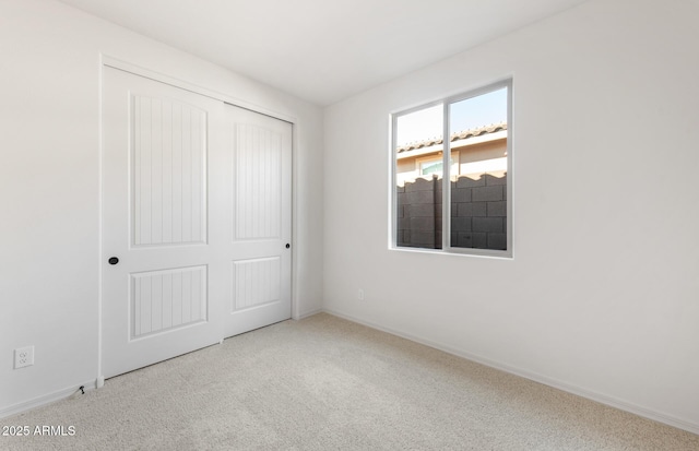 unfurnished bedroom with light carpet, a closet, and baseboards