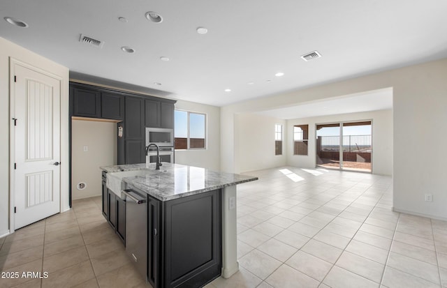 kitchen with dark cabinetry, appliances with stainless steel finishes, a center island with sink, and visible vents