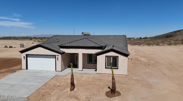 view of front facade featuring concrete driveway, a tile roof, a mountain view, an attached garage, and stucco siding