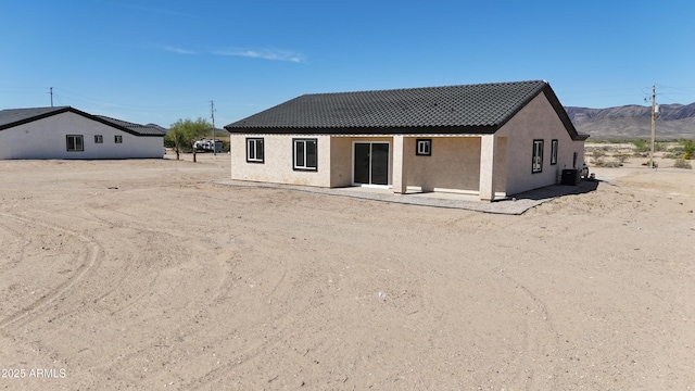back of property with a mountain view, stucco siding, and a tiled roof