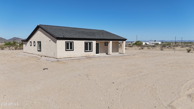 back of house with stucco siding and a tile roof
