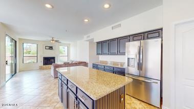 kitchen featuring a kitchen island, dark brown cabinets, stainless steel refrigerator with ice dispenser, ceiling fan, and light stone counters