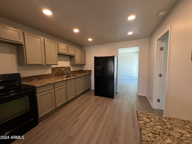 kitchen with dark stone counters, black appliances, hardwood / wood-style flooring, sink, and gray cabinetry