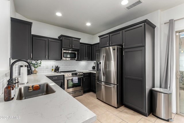 kitchen with appliances with stainless steel finishes, light tile patterned floors, decorative backsplash, sink, and light stone counters