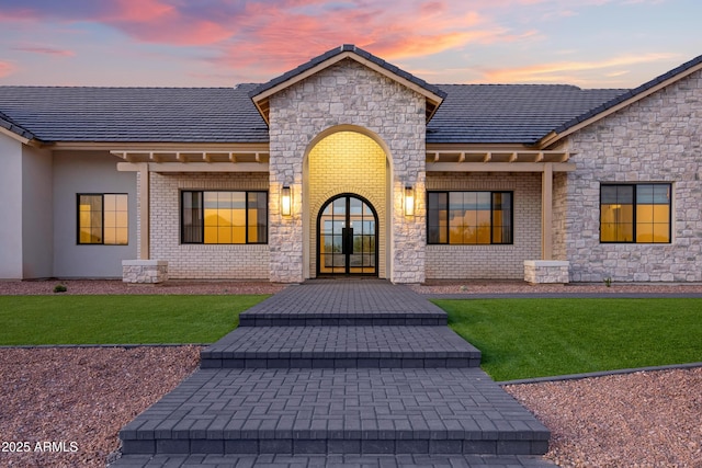 10760 W Golddust Dr, Queen Creek, AZ 85144 - exterior entry at dusk featuring a lawn, stone siding, and french doors