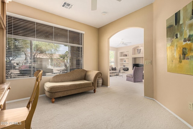 living area featuring light carpet, built in features, and ceiling fan