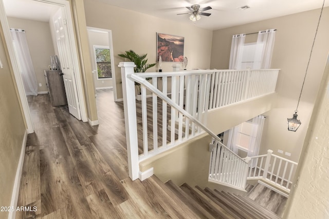 staircase with wood finished floors, a ceiling fan, and baseboards