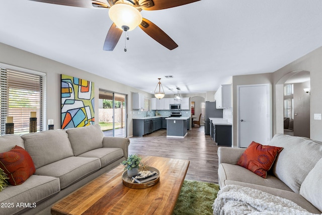 living area featuring arched walkways, ceiling fan, light wood-type flooring, and visible vents