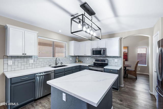 kitchen featuring arched walkways, a center island, stainless steel appliances, tasteful backsplash, and a sink