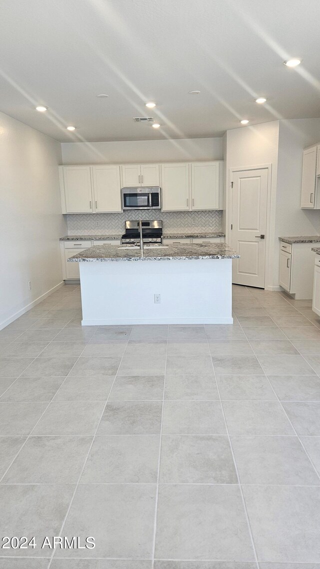 kitchen with appliances with stainless steel finishes, an island with sink, and light tile patterned floors