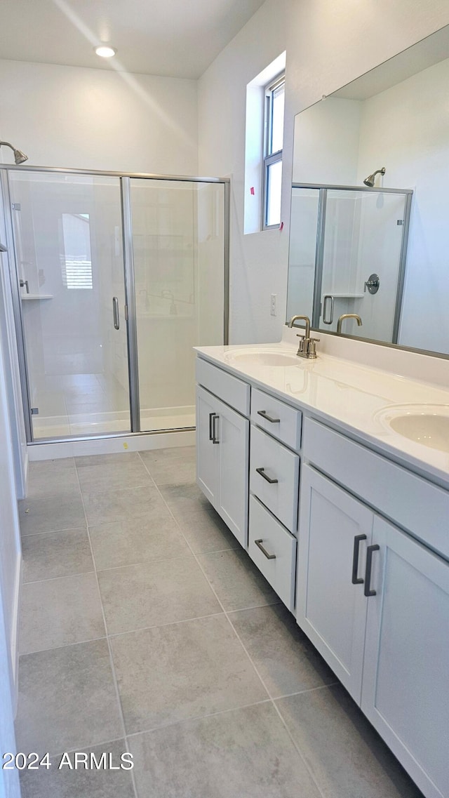 bathroom featuring a shower with shower door, dual vanity, and tile patterned floors