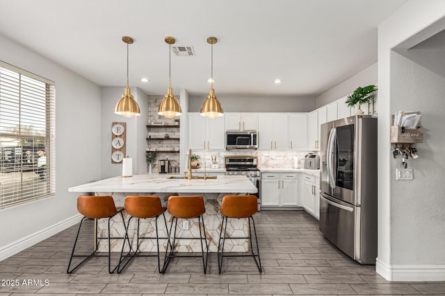 kitchen with appliances with stainless steel finishes, white cabinetry, hanging light fixtures, backsplash, and a kitchen breakfast bar