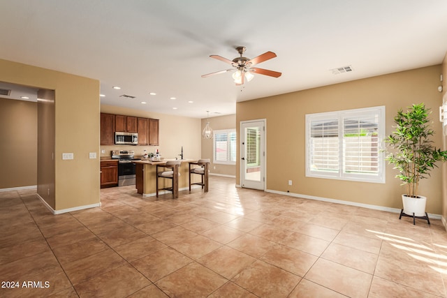 kitchen with stainless steel appliances, a center island with sink, a breakfast bar, light tile patterned floors, and decorative light fixtures