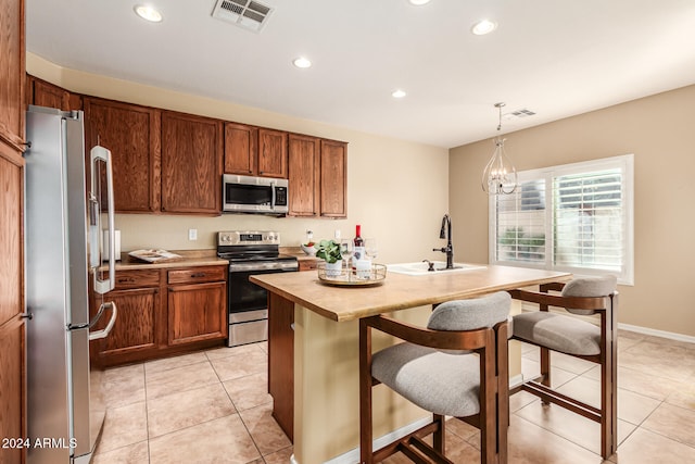 kitchen featuring a center island with sink, appliances with stainless steel finishes, light tile patterned floors, pendant lighting, and an inviting chandelier