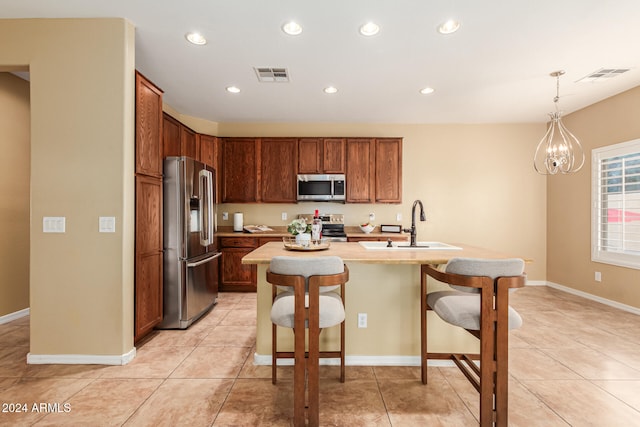 kitchen with sink, light tile patterned floors, a kitchen island with sink, appliances with stainless steel finishes, and decorative light fixtures