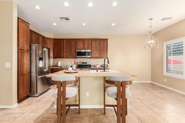 kitchen featuring stainless steel appliances, decorative light fixtures, sink, a breakfast bar area, and a kitchen island with sink