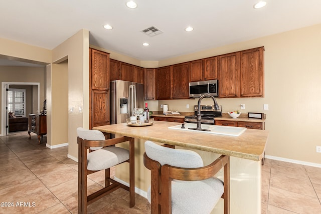 kitchen featuring a kitchen bar, stainless steel appliances, a kitchen island with sink, and light tile patterned floors