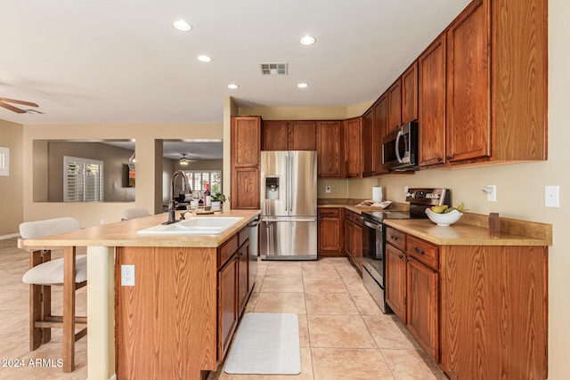 kitchen with a center island with sink, stainless steel appliances, light tile patterned floors, sink, and a breakfast bar