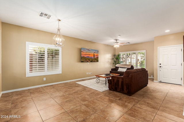 tiled living room with ceiling fan with notable chandelier