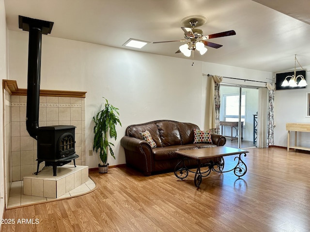 living room featuring ceiling fan with notable chandelier, light hardwood / wood-style floors, and a wood stove