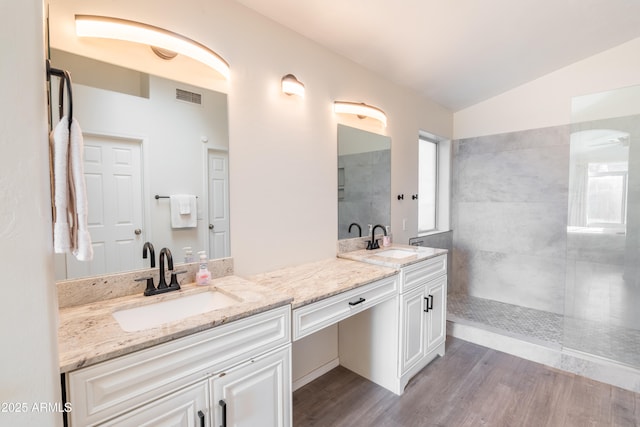 bathroom with vanity, hardwood / wood-style flooring, tiled shower, and lofted ceiling