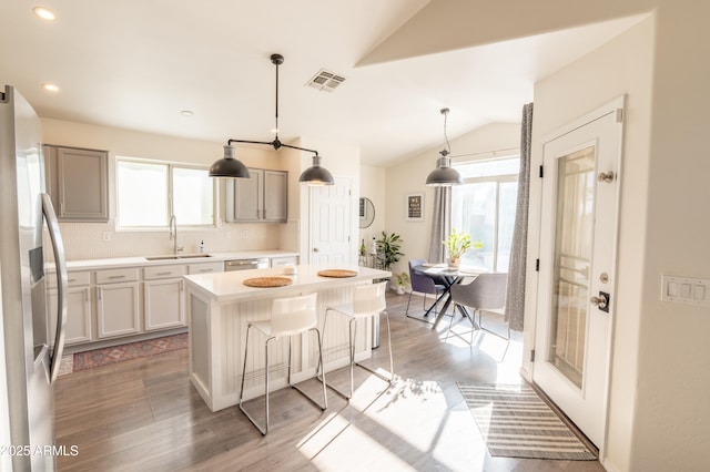 kitchen with vaulted ceiling, appliances with stainless steel finishes, sink, decorative light fixtures, and a kitchen island