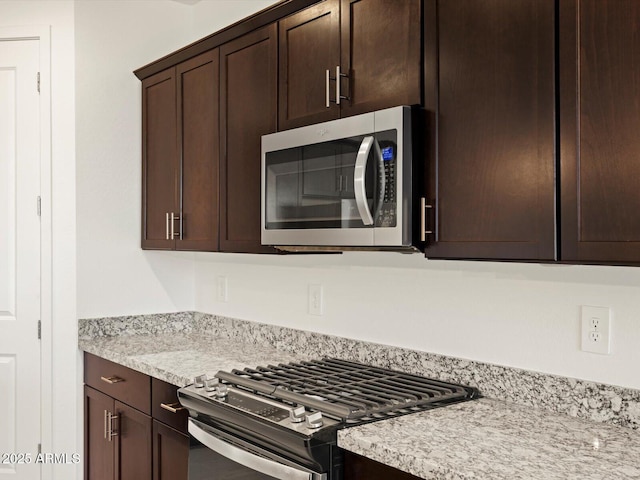 kitchen featuring stainless steel appliances, light stone countertops, and dark brown cabinets