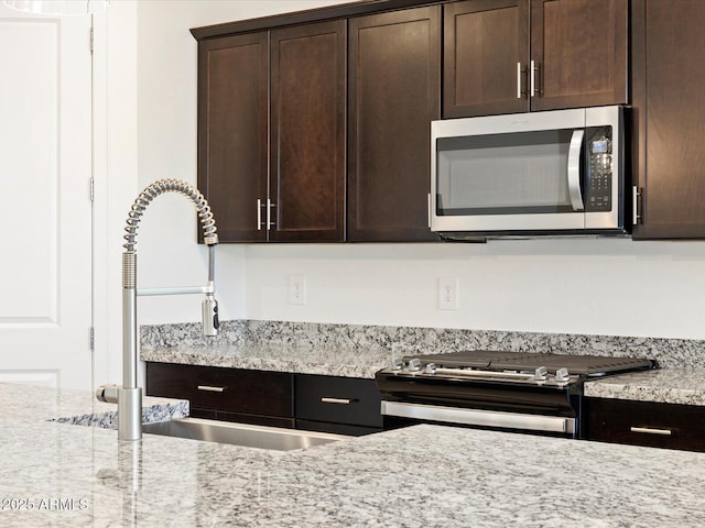 kitchen with stainless steel appliances, sink, light stone counters, and dark brown cabinetry