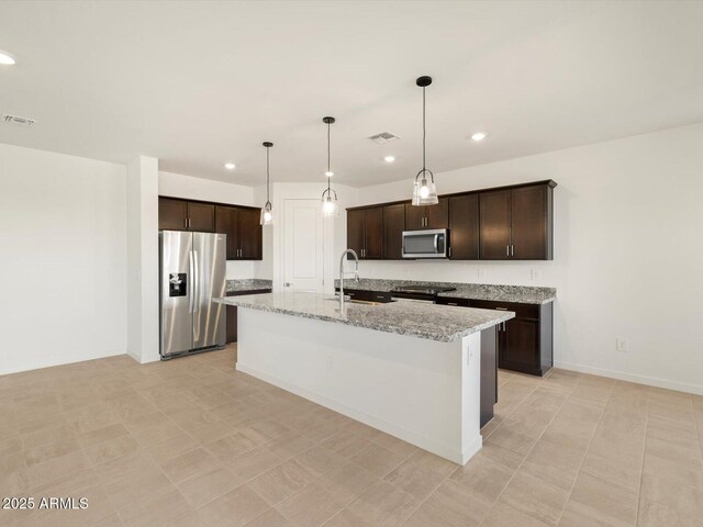 kitchen with light stone countertops, pendant lighting, stainless steel appliances, a kitchen island with sink, and dark brown cabinets