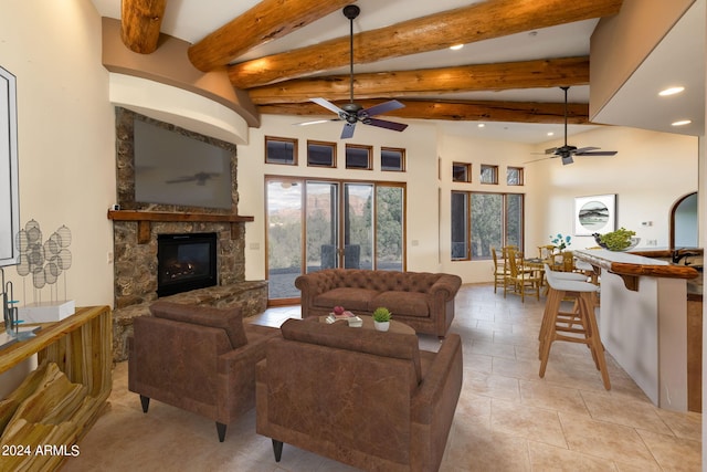 living room featuring ceiling fan, a stone fireplace, and beamed ceiling