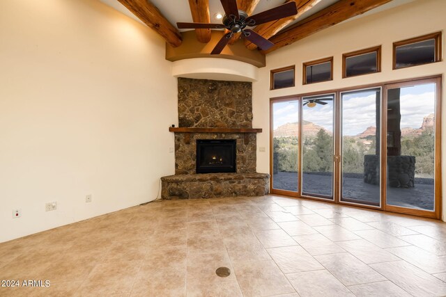 unfurnished living room featuring beamed ceiling, ceiling fan, a stone fireplace, and a mountain view