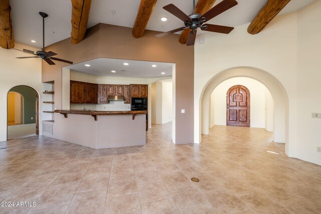 kitchen featuring black microwave, a kitchen breakfast bar, kitchen peninsula, ceiling fan, and beam ceiling