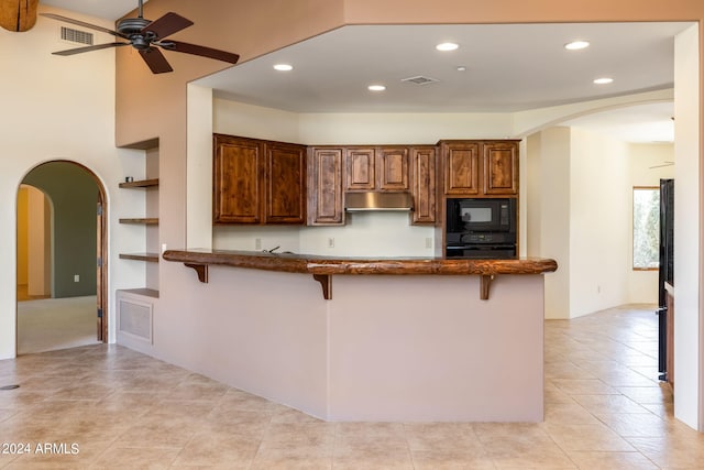 kitchen with a breakfast bar, black microwave, ceiling fan, kitchen peninsula, and built in shelves