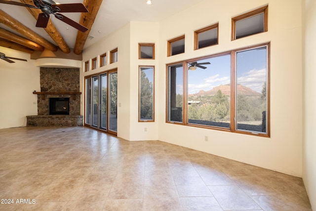 unfurnished living room featuring light tile patterned flooring, a stone fireplace, beamed ceiling, ceiling fan, and a high ceiling