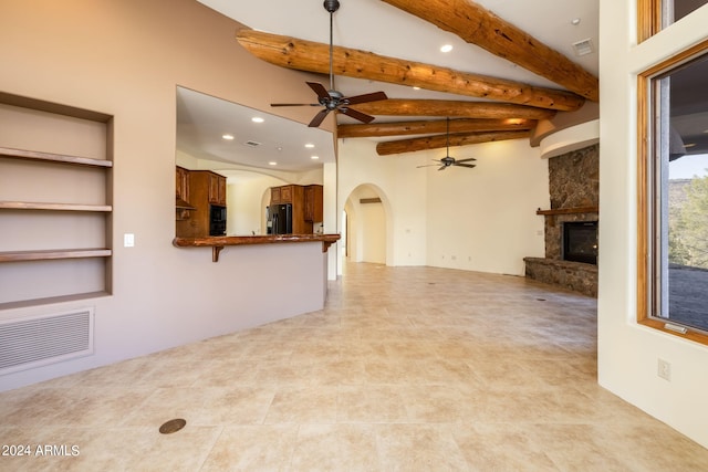 unfurnished living room featuring beam ceiling, light tile patterned floors, a stone fireplace, and ceiling fan