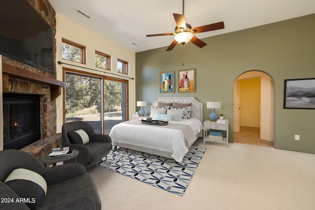 carpeted bedroom with ceiling fan, access to exterior, and a stone fireplace