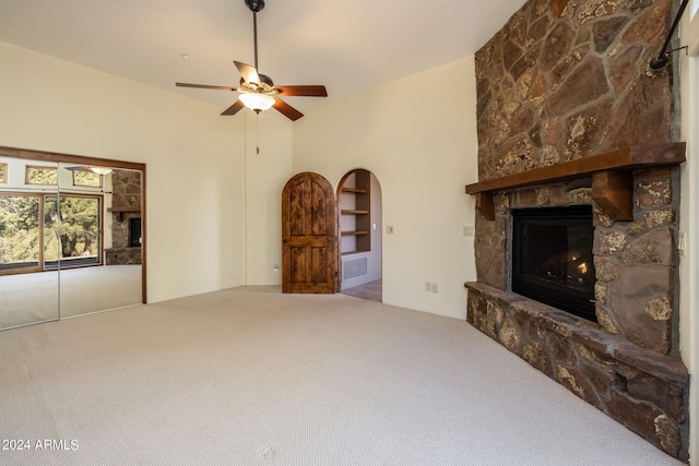 carpeted living room with a stone fireplace, a towering ceiling, and ceiling fan