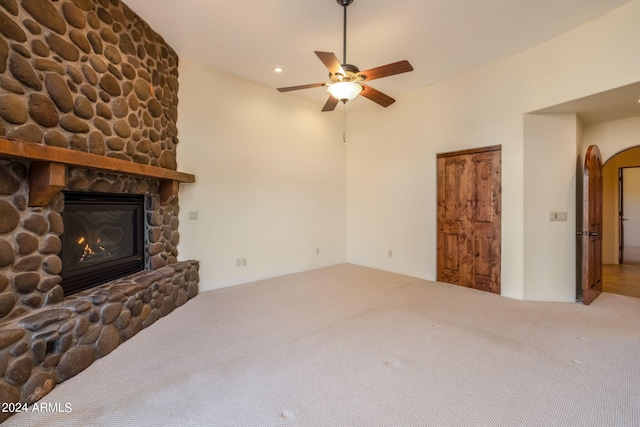 unfurnished living room featuring ceiling fan, a stone fireplace, and carpet