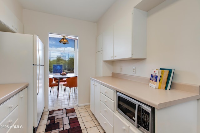 kitchen featuring stainless steel microwave, light tile patterned floors, white cabinetry, light countertops, and freestanding refrigerator