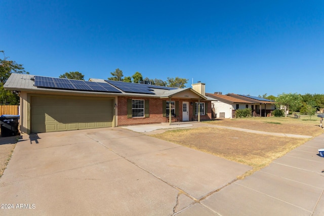 ranch-style home featuring a garage, driveway, solar panels, a chimney, and brick siding