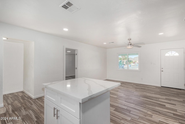 kitchen with white cabinetry, ceiling fan, light stone counters, light hardwood / wood-style flooring, and a kitchen island