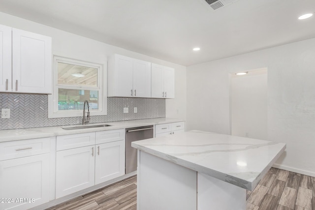 kitchen featuring light stone countertops, stainless steel dishwasher, sink, a center island, and white cabinetry