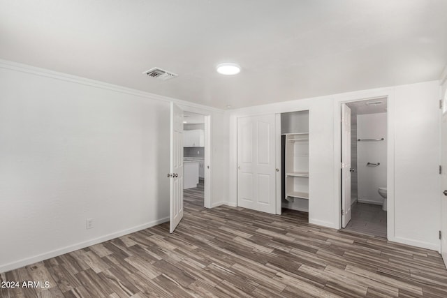 unfurnished bedroom with a closet, dark wood-type flooring, and ensuite bath